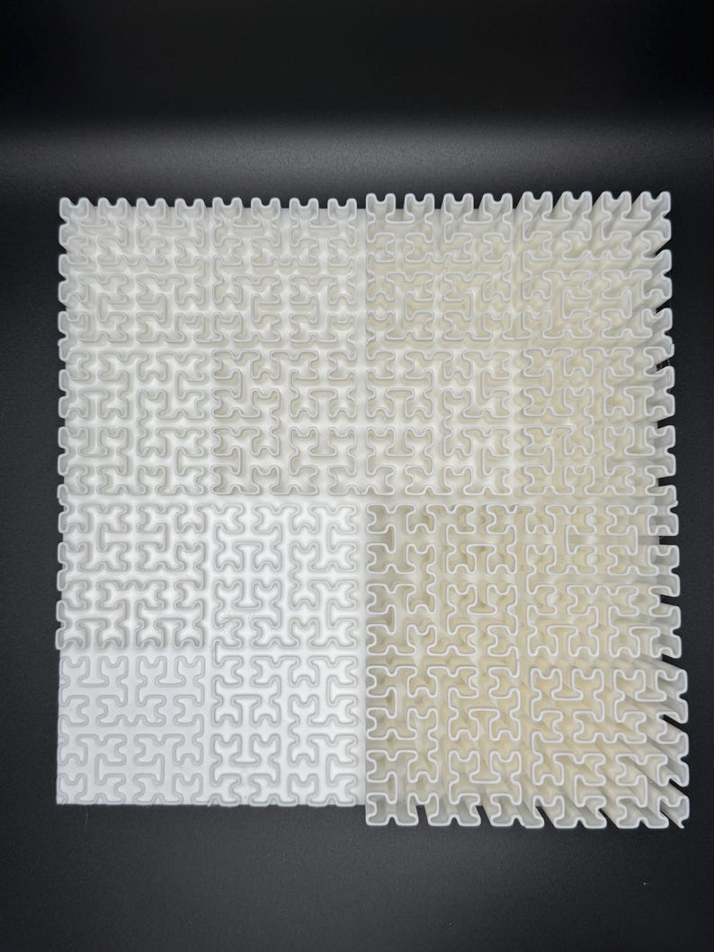 May include: A white plastic puzzle with a grid pattern. The puzzle is made up of small, interlocking pieces. The puzzle is divided into four sections, with each section having a different pattern.
