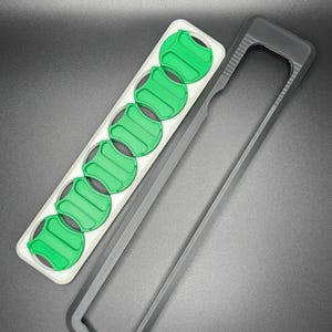 May include: A black plastic case with a white and green insert. The insert has eight slots for holding small round objects.