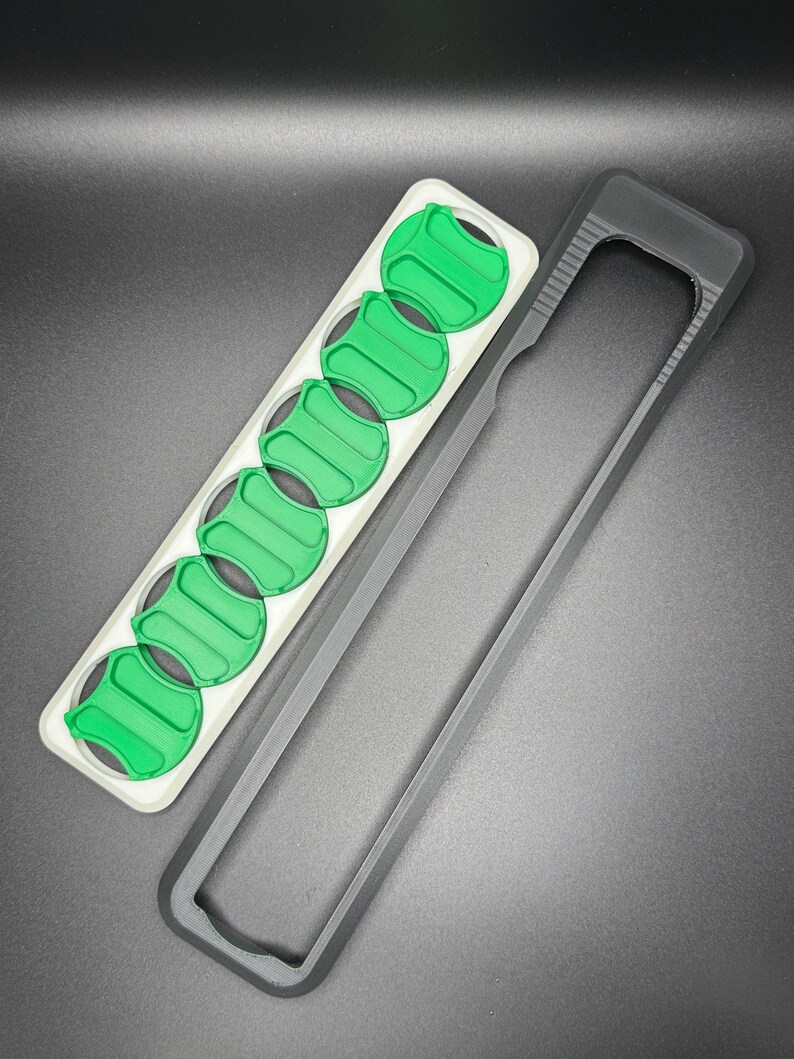 May include: A black plastic case with a white and green insert. The insert has eight slots for holding small round objects.