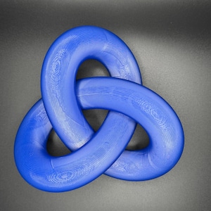 May include: A blue, three-dimensional knot, resembling a Celtic trinity knot, is made of a smooth, shiny material. The knot is isolated against a dark gray background.