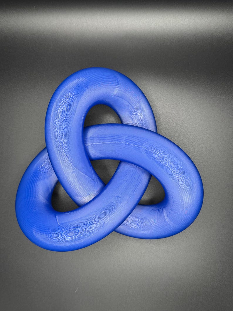 May include: A blue, three-dimensional knot, resembling a Celtic trinity knot, is made of a smooth, shiny material. The knot is isolated against a dark gray background.
