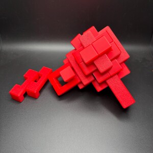 May include: A red 3D puzzle made of interlocking blocks. The puzzle is in the shape of a key and is made of many small, square blocks.