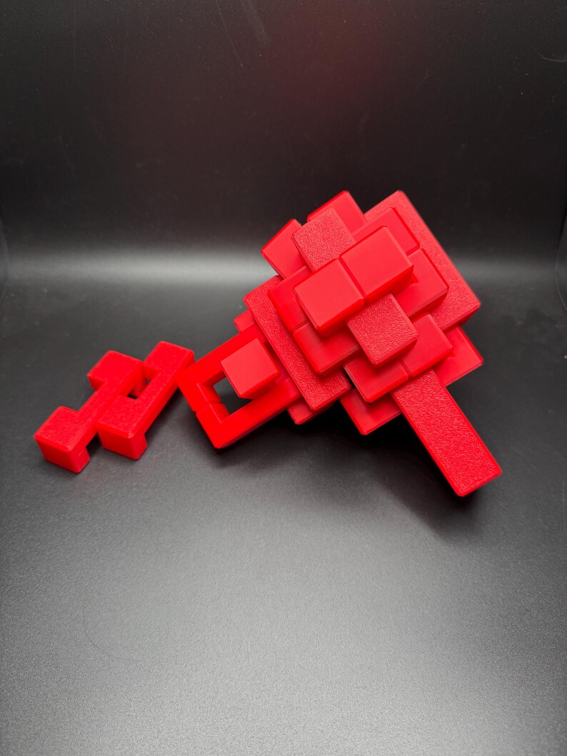 May include: A red 3D puzzle made of interlocking blocks. The puzzle is in the shape of a key and is made of many small, square blocks.