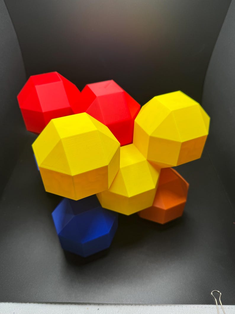 May include: A group of six geometric shapes, each with a different color. The shapes are red, yellow, blue, and orange. They are arranged in a cluster, with the yellow shape in the center.