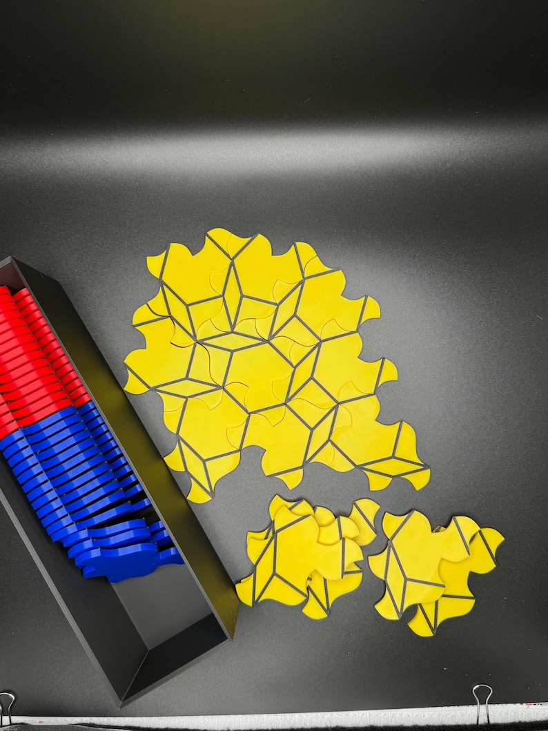 May include: A yellow geometric puzzle with black lines. The puzzle pieces are arranged in a circular pattern. The puzzle is in a black tray with blue and red puzzle pieces.
