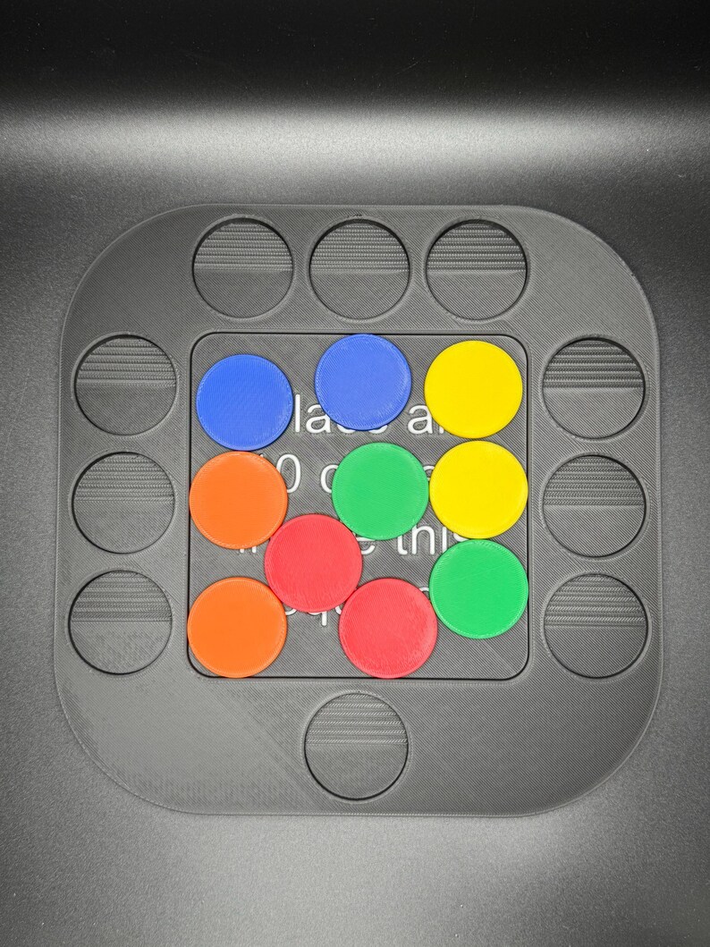 K&ouml;nnte beinhalten: Ein graues Puzzlespielbrett mit kreisf&ouml;rmigen Aussparungen und einem zentralen Raster. Das Raster enth&auml;lt farbige kreisf&ouml;rmige Teile in Blau, Orange, Rot, Gr&uuml;n und Gelb. Text ist auf dem Brett sichtbar. Ein lustiges und ansprechendes Spiel.