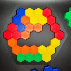 May include: A hexagonal puzzle with pieces in red, orange, yellow, green, and blue. The pieces are arranged in a circular pattern with a gap in the middle.