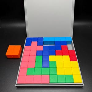 May include: A wooden box with a lid open, revealing a colorful puzzle made of small square blocks. The puzzle is arranged in a pattern with blocks of red, blue, green, yellow, and orange.