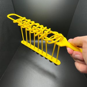 Pode incluir: Um brinquedo de pl&aacute;stico amarelo com uma s&eacute;rie de la&ccedil;os que podem ser movidos ao longo de uma s&eacute;rie de hastes de metal. O brinquedo &eacute; segurado na m&atilde;o.