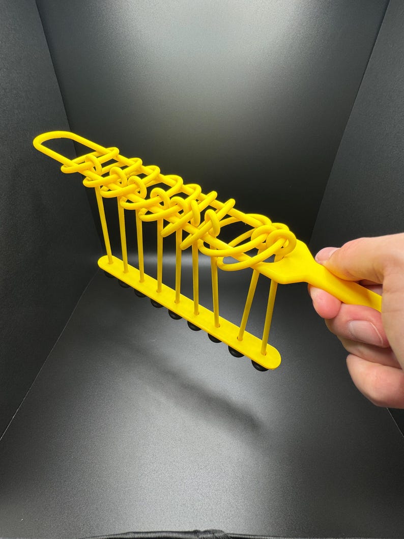 Pode incluir: Um brinquedo de pl&aacute;stico amarelo com uma s&eacute;rie de la&ccedil;os que podem ser movidos ao longo de uma s&eacute;rie de hastes de metal. O brinquedo &eacute; segurado na m&atilde;o.