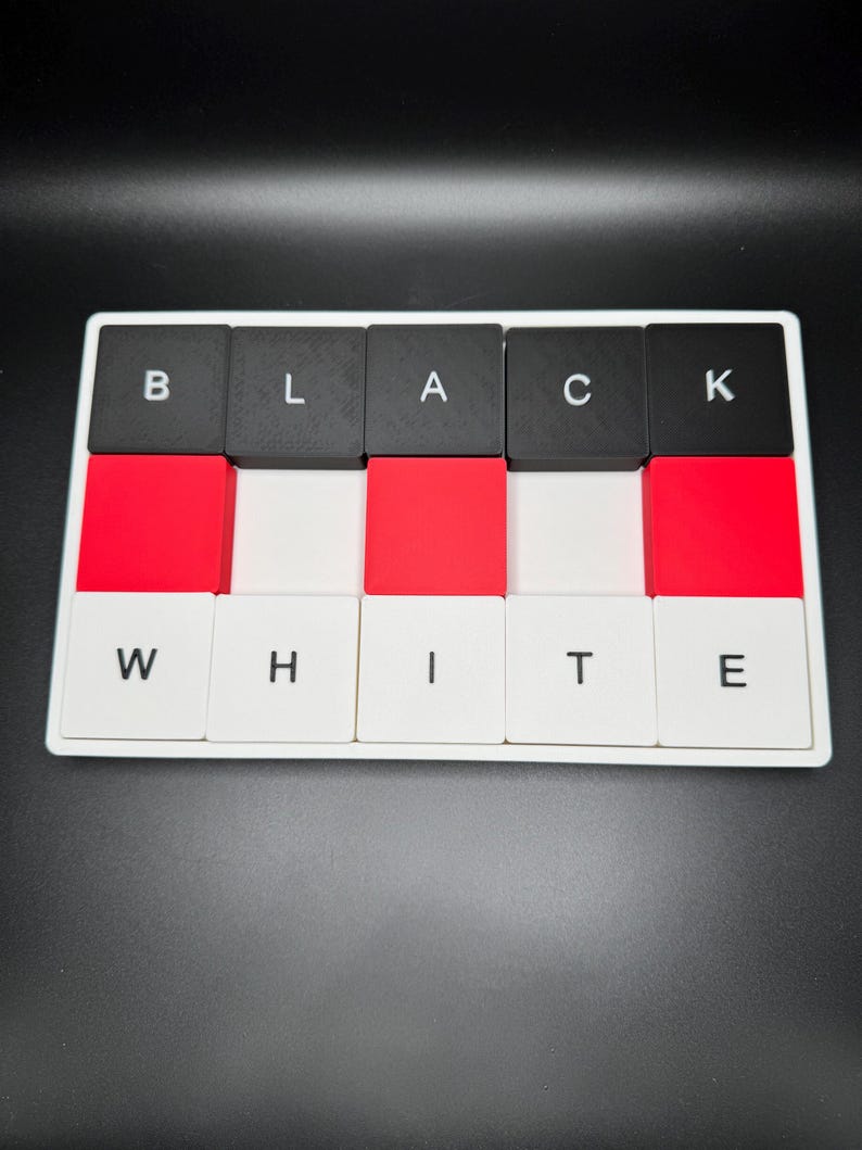May include: A rectangular game board with black, red, and white tiles. The top row spells "BLACK" and the bottom row spells "WHITE". The tiles are arranged in a grid pattern, with the letters in black on a white background.