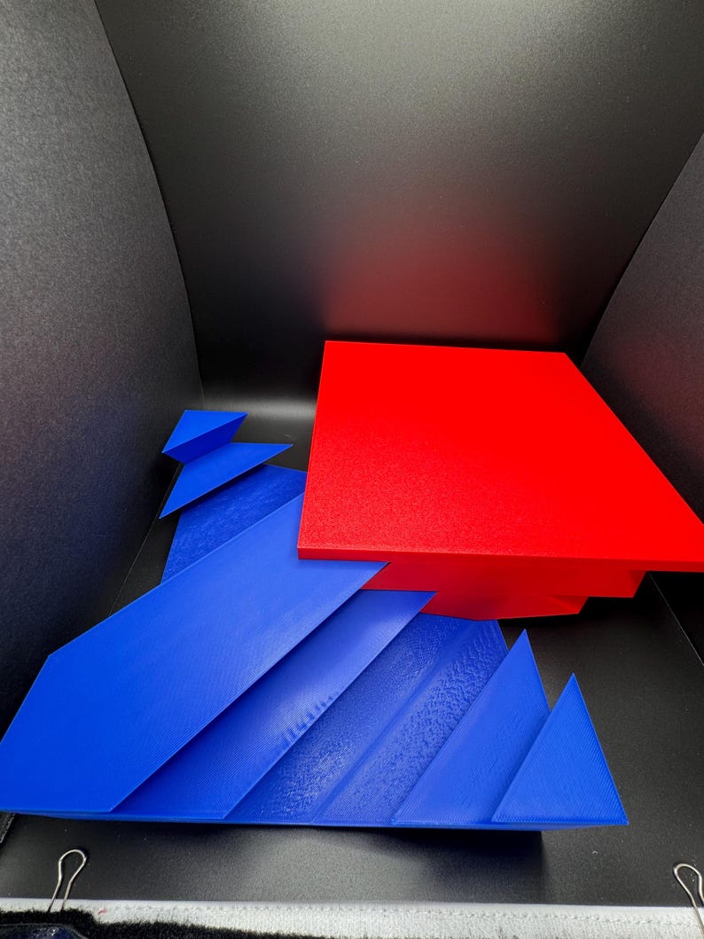 May include: A red and blue geometric shape made of cardboard. The red shape is a square and the blue shape is a series of triangles.