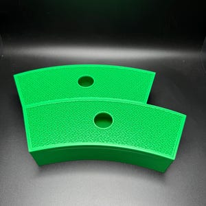May include: Two bright green, curved, textured trays with a circular hole in the center. The trays are stacked on top of each other, with a dark background.
