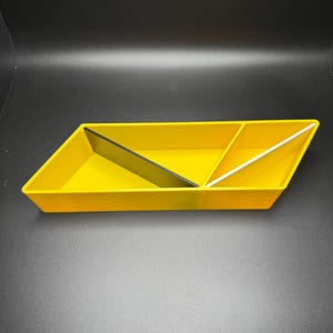 May include: A yellow, triangular-shaped tray with three compartments. The compartments are divided by black and white dividers.