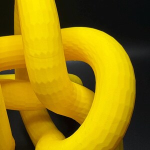 May include: A yellow 3D printed abstract sculpture with a smooth, rounded surface. The sculpture is made up of multiple interconnected loops.