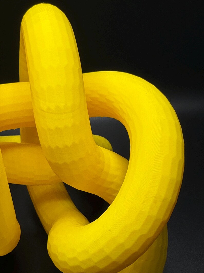 May include: A yellow 3D printed abstract sculpture with a smooth, rounded surface. The sculpture is made up of multiple interconnected loops.