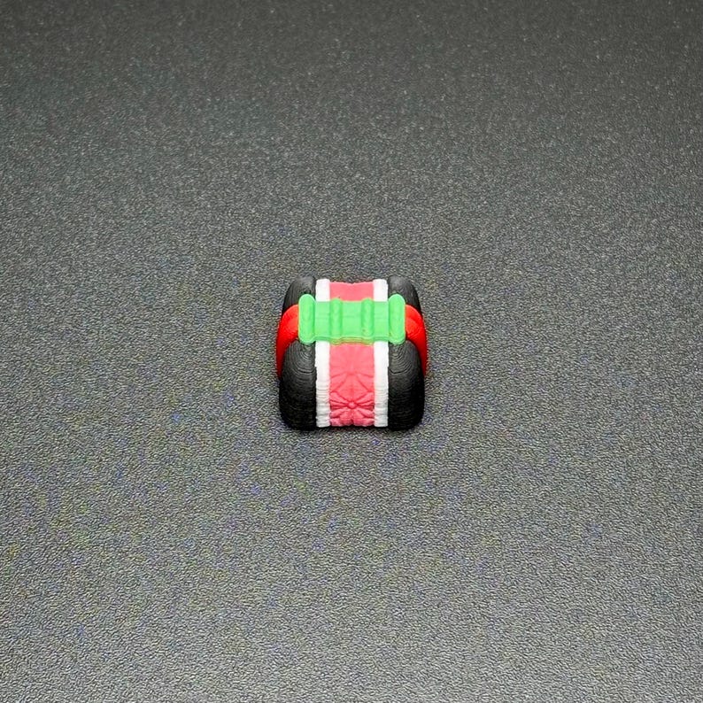 May include: A small, black and red toy with a green stripe. The toy is shaped like a box with rounded edges.