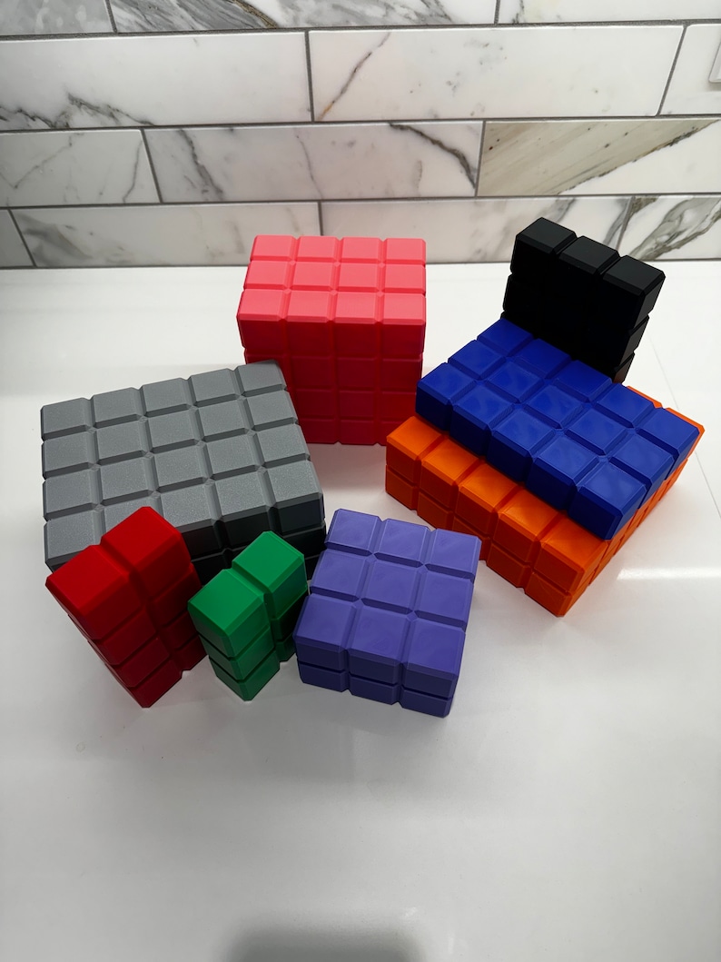 May include: A set of nine colorful, square-shaped blocks with a textured surface. The blocks are made of a soft, pliable material and are arranged in a pyramid shape. The blocks are in various colors, including red, orange, yellow, green, blue, purple, and gray.