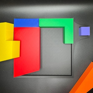 Op de afbeelding: Een set geometrische vormen in verschillende kleuren, waaronder een gele, rode, blauwe, groene en paarse blok, gerangschikt op een zwart oppervlak.