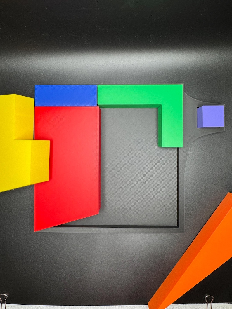 Op de afbeelding: Een set geometrische vormen in verschillende kleuren, waaronder een gele, rode, blauwe, groene en paarse blok, gerangschikt op een zwart oppervlak.