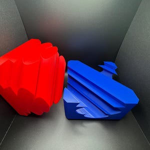 May include: Two geometric shapes, one red and one blue, made of a smooth, solid material. The red shape is a multi-sided, rounded object. The blue shape is a flat, multi-sided object with a curved edge.