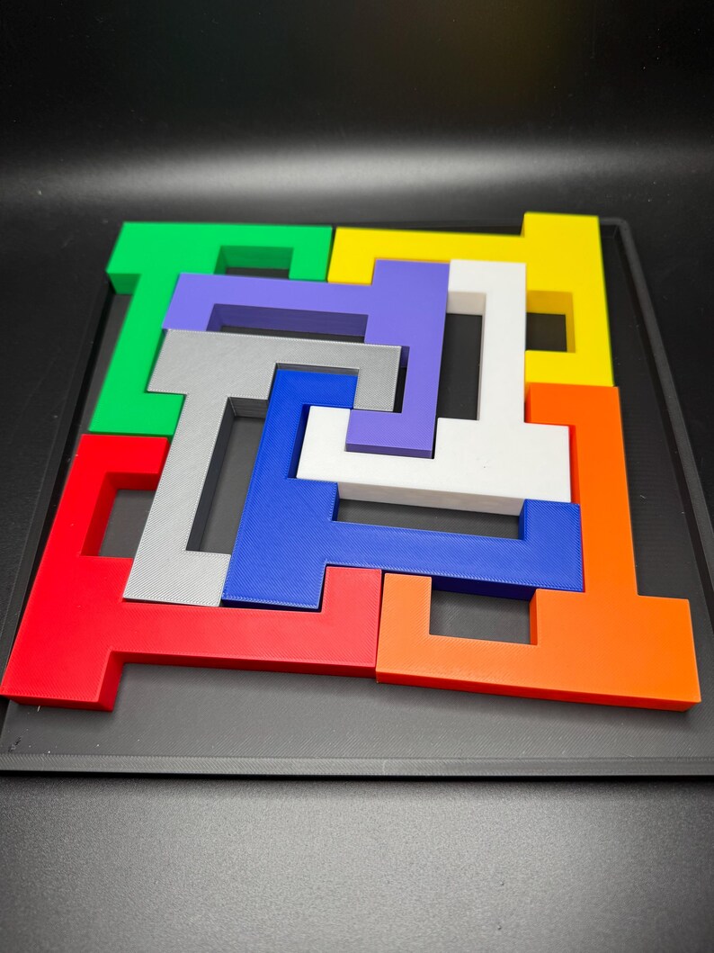 Op de afbeelding: Een kleurrijke puzzel met zeven stukken, elk in de vorm van een T, past samen om een vierkant te vormen. De stukken zijn rood, oranje, geel, groen, blauw, paars en grijs.