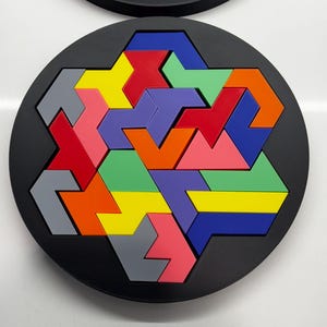 May include: A circular puzzle with a black background and a colorful geometric design. The puzzle pieces are made of different colors, including red, orange, yellow, green, blue, purple, and gray.