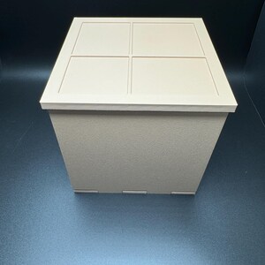 May include: A beige square box with a lid. The lid has four square indentations.