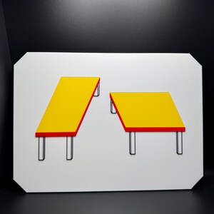 May include: A white rectangular sign featuring two yellow tables with red trim and black legs. One table is rectangular and angled, while the other is square. The background is black.