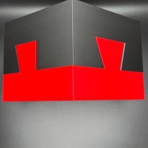 May include: A black and red cube with a geometric design. The cube is made of cardboard and has a red bottom and black top.