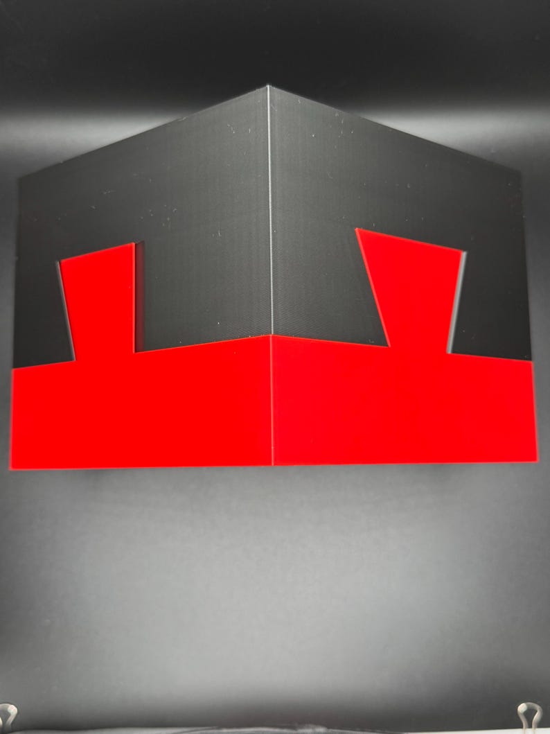 May include: A black and red cube with a geometric design. The cube is made of cardboard and has a red bottom and black top.