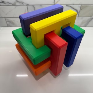 May include: A colorful wooden puzzle with interlocking pieces in red, green, blue, yellow, and orange. The puzzle is in the shape of a cube.