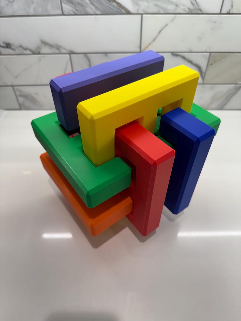 May include: A colorful wooden puzzle with interlocking pieces in red, green, blue, yellow, and orange. The puzzle is in the shape of a cube.