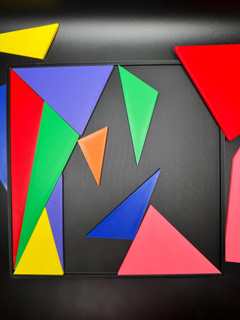 May include: A colorful geometric puzzle with pieces in red, green, blue, yellow, orange, and pink. The pieces are arranged on a black surface to form a square.