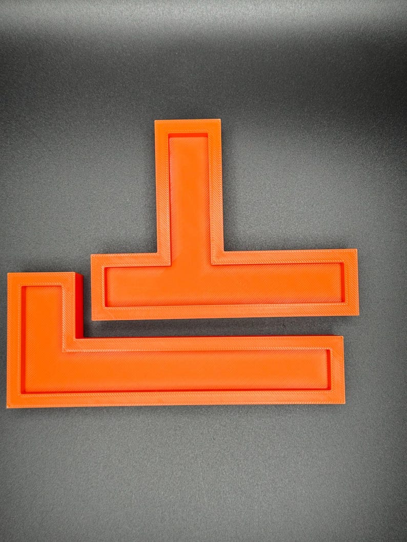 May include: Two orange plastic L-shaped rulers stacked on top of each other.