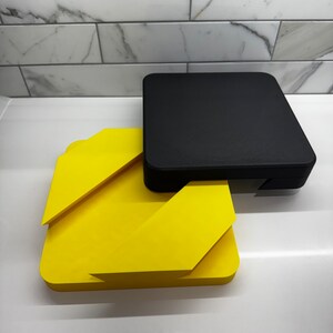 May include: A yellow and black geometric shape made of two pieces. The top piece is black and the bottom piece is yellow.