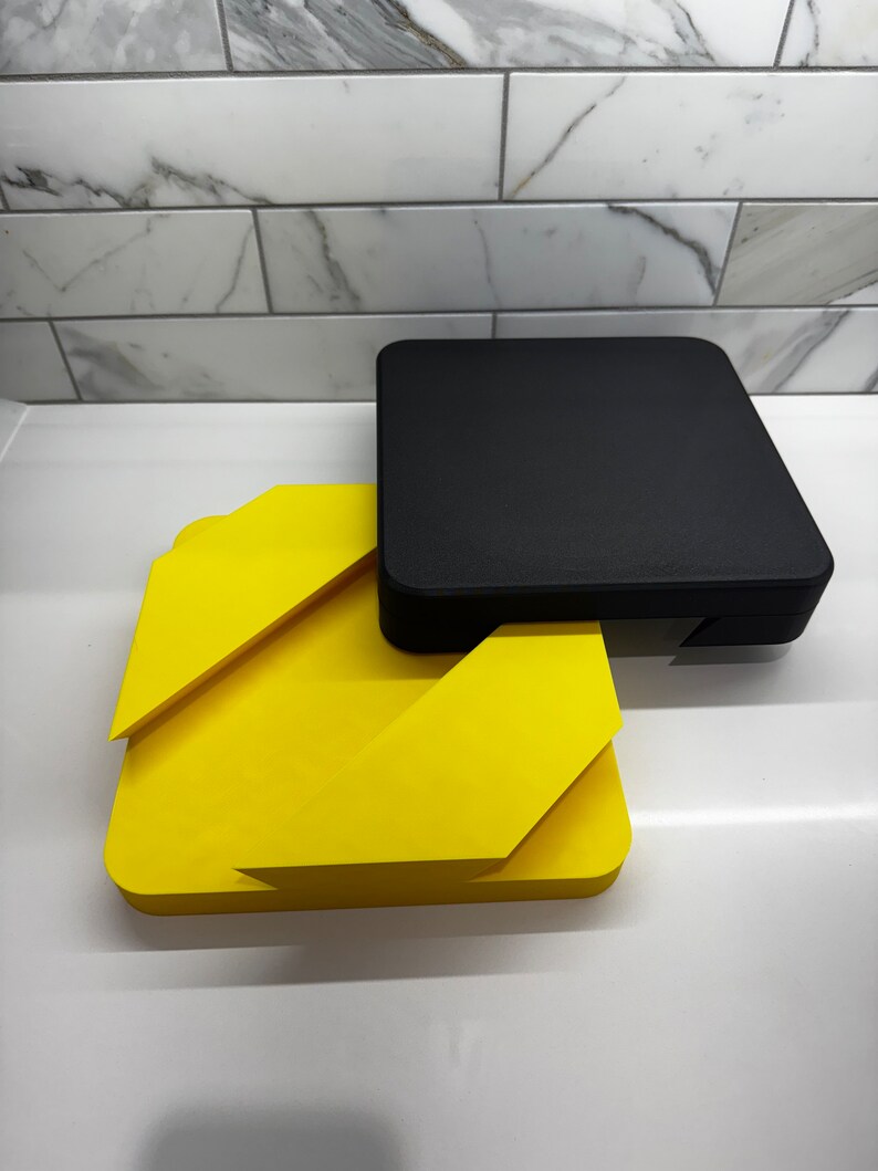 May include: A yellow and black geometric shape made of two pieces. The top piece is black and the bottom piece is yellow.