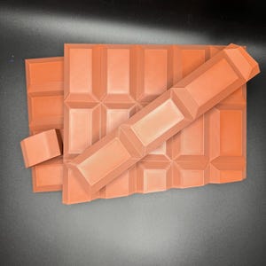 May include: A stack of four rectangular chocolate bars with a textured surface. The bars are arranged in a staggered pattern, with the top bar partially covering the bars below.