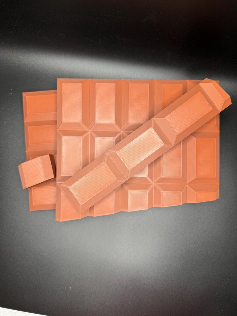 May include: A stack of four rectangular chocolate bars with a textured surface. The bars are arranged in a staggered pattern, with the top bar partially covering the bars below.