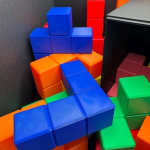 Może przedstawiać: Kolorowy zestaw blok&oacute;w w kształcie Tetris w kolorze niebieskim, zielonym, pomarańczowym i czerwonym. Bloki są ułożone w losowym wzorze, tworząc wizualnie atrakcyjny i abstrakcyjny projekt.