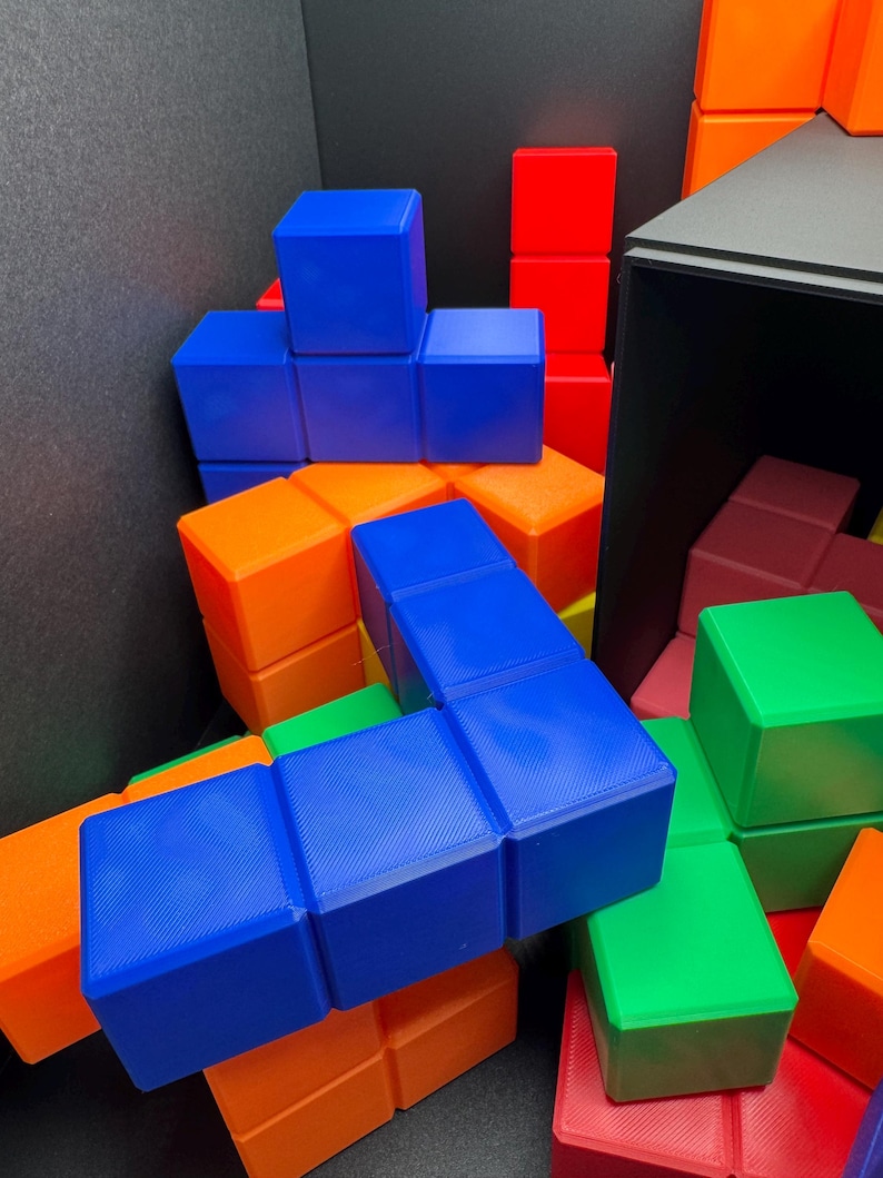 Może przedstawiać: Kolorowy zestaw blok&oacute;w w kształcie Tetris w kolorze niebieskim, zielonym, pomarańczowym i czerwonym. Bloki są ułożone w losowym wzorze, tworząc wizualnie atrakcyjny i abstrakcyjny projekt.