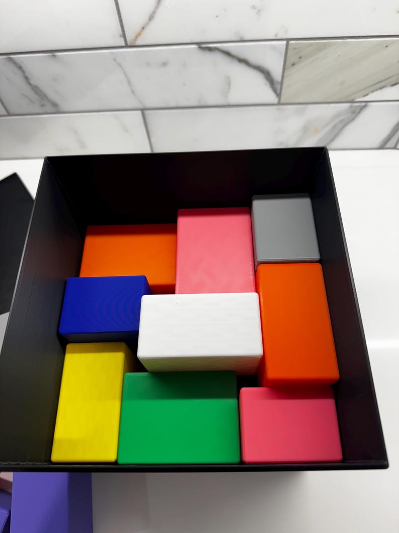 May include: A black box filled with colorful blocks. The blocks are arranged in a pattern and include red, orange, yellow, green, blue, white, pink, and gray.