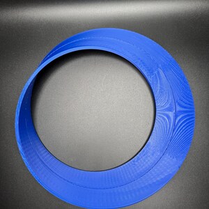 May include: A blue plastic ring with a smooth, rounded surface. The ring is made of two overlapping circles, creating a unique and modern design.