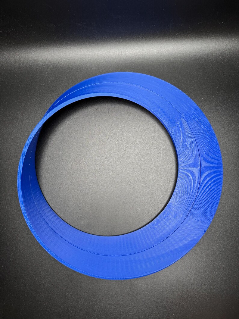 May include: A blue plastic ring with a smooth, rounded surface. The ring is made of two overlapping circles, creating a unique and modern design.