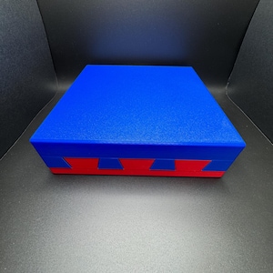 May include: A blue box with a red and blue geometric pattern on the bottom. The box is made of a smooth, textured material.