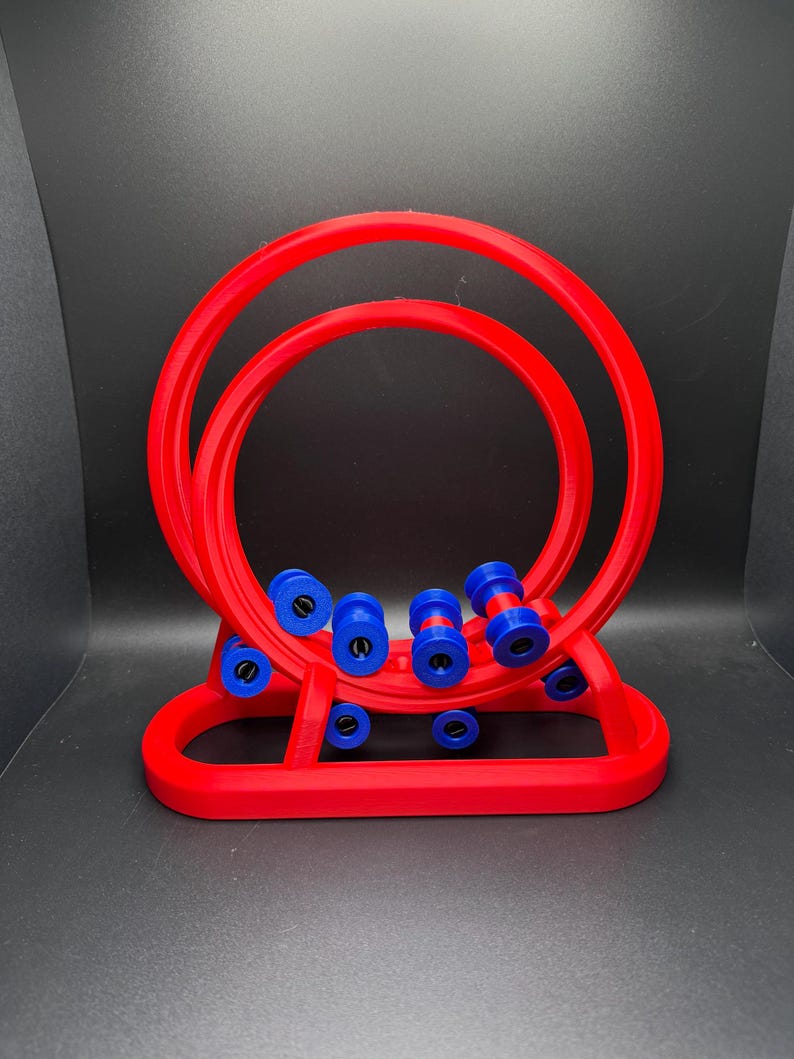 May include: A red, 3D-printed abacus-style toy with two large circular frames and a series of blue and red beads. The base is also red, and the toy is set against a dark background.