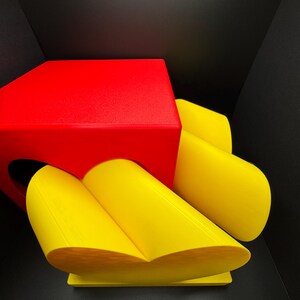 Pode incluir: Um cubo vermelho com um objeto amarelo em forma de cora&ccedil;&atilde;o no topo. O objeto em forma de cora&ccedil;&atilde;o &eacute; feito de duas pe&ccedil;as curvas que se juntam.