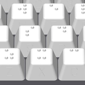 May include: A close-up of a white keyboard with braille lettering on the keys.