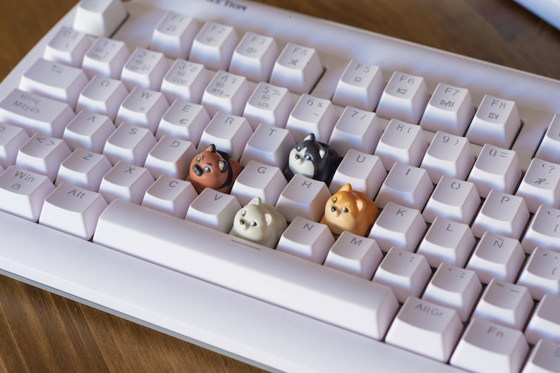 May include: A white mechanical keyboard with custom keycaps shaped like cartoon dogs. The keycaps are various colors, including brown, black, and cream. The keyboard has a standard layout with white keys and black lettering.