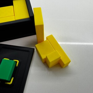 Pu&ograve; includere: Un puzzle di legno giallo con pezzi che si incastrano per formare una scatola. Il puzzle &egrave; parzialmente assemblato, con alcuni pezzi ancora fuori dalla scatola.